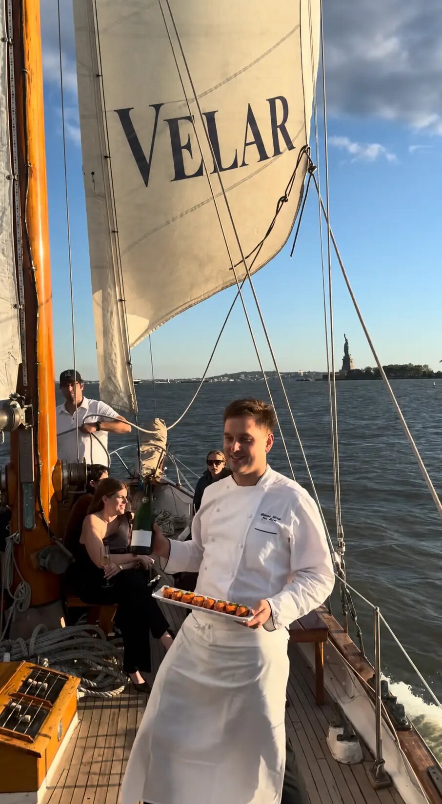 Aboard a sailboat with a VELAR sail: a chef serves guests facing New York Harbor