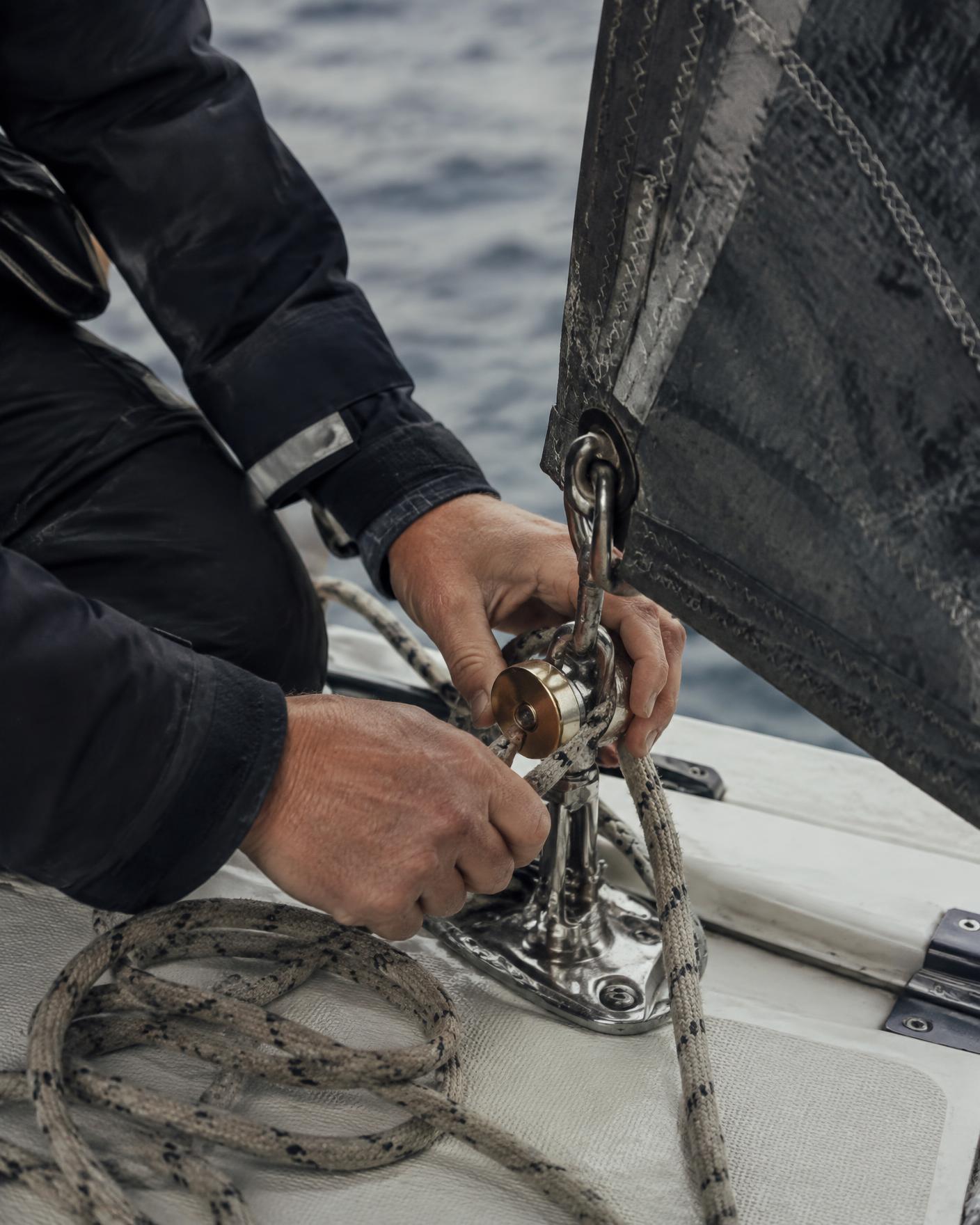 Hands adjusting a deck fitting beside the sailcloth